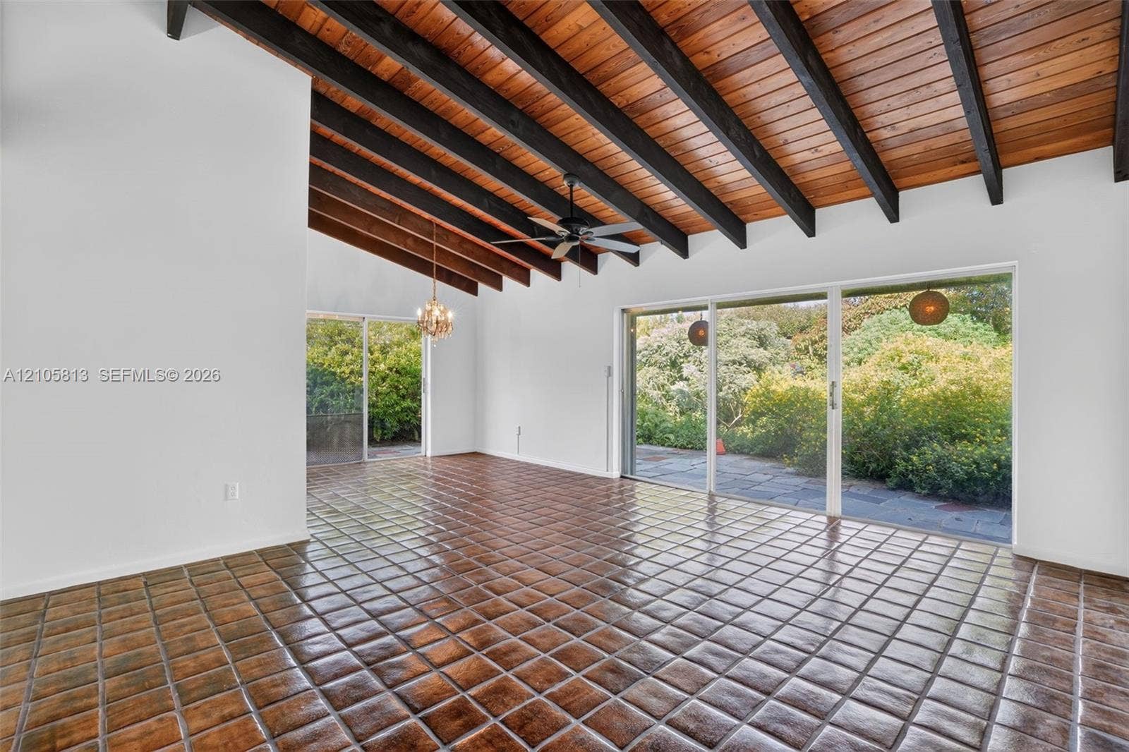 Vaulted ceiling featuring exposed wood beams and wood planking, terra-cotta tile flooring, and oversized sliding glass doors