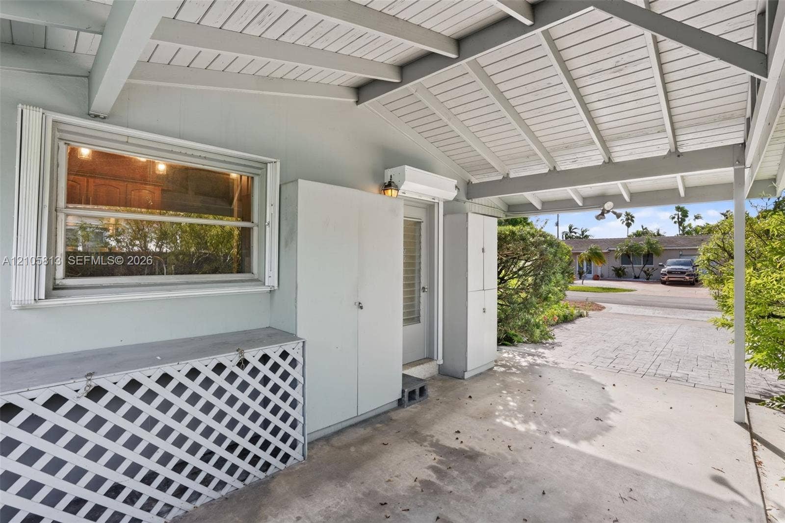 Covered carport featuring a concrete floor, built-in storage cabinetry, decorative lattice screen, exposed beam ceiling, and a concrete driveway