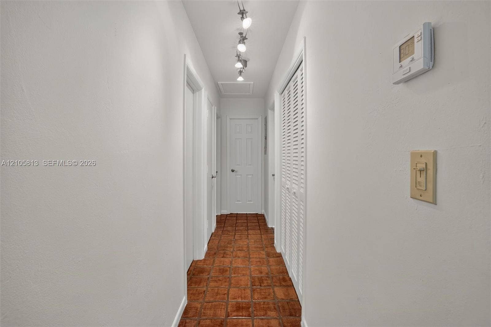 Interior hallway featuring terra cotta tile flooring, multi-panel doors, louvered closet doors, and adjustable track lighting