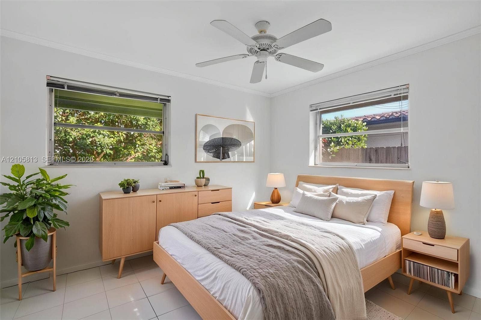 Neutral-toned interior space featuring light-reflective ceramic tile flooring, two expansive windows, and a central white ceiling fan