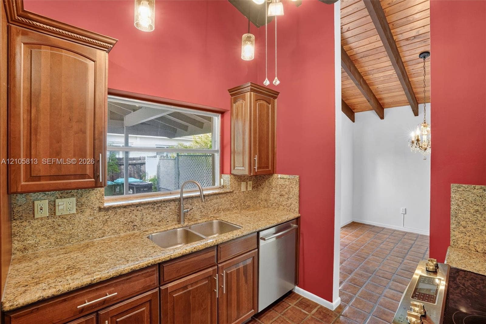 Kitchen featuring natural wood cabinetry, stone-surface countertops, dual-basin stainless steel sink, tile flooring, and vaulted ceiling with exposed timber beams
