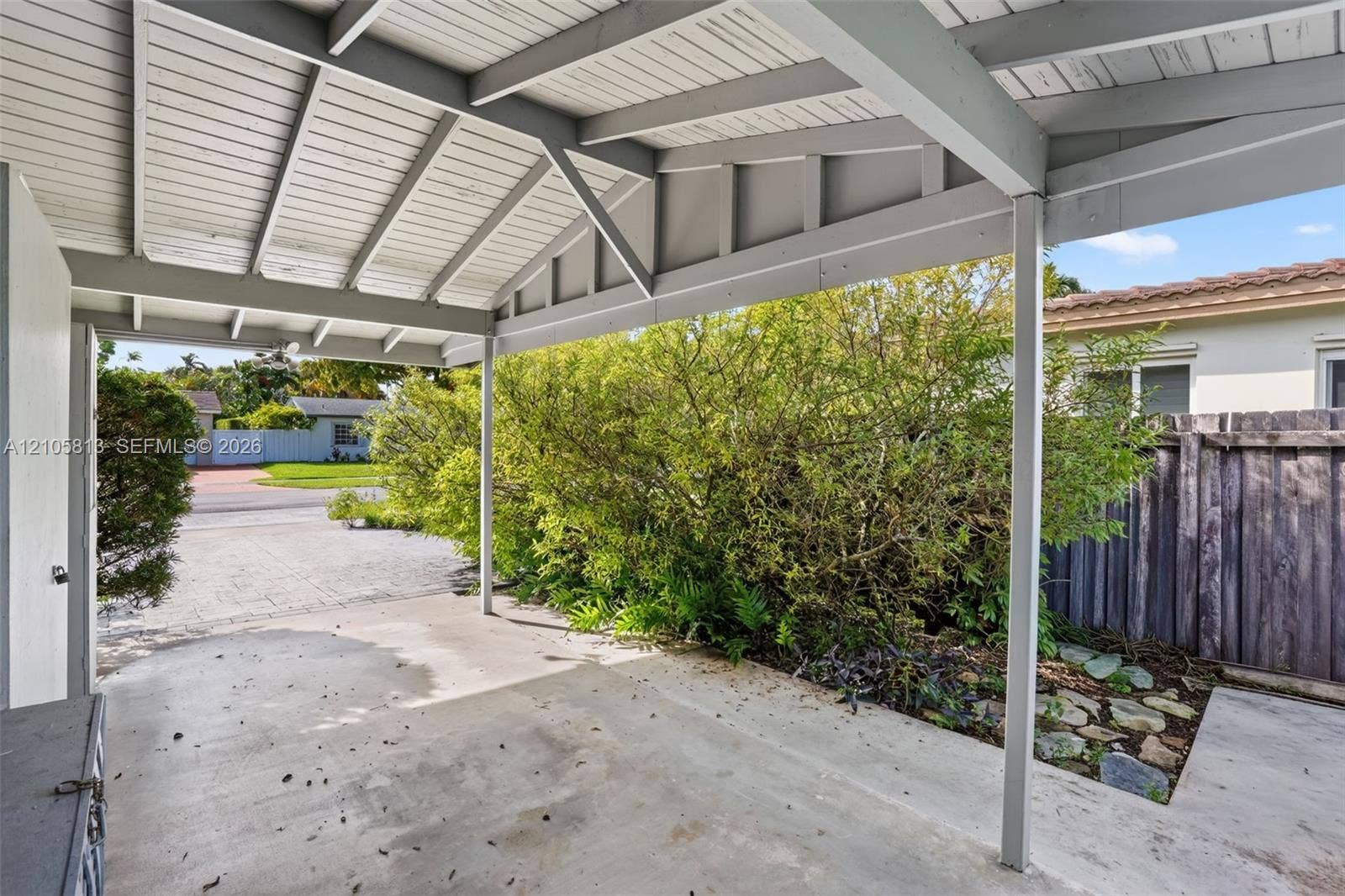 Covered carport with a gabled ceiling, concrete flooring, and perimeter privacy fencing