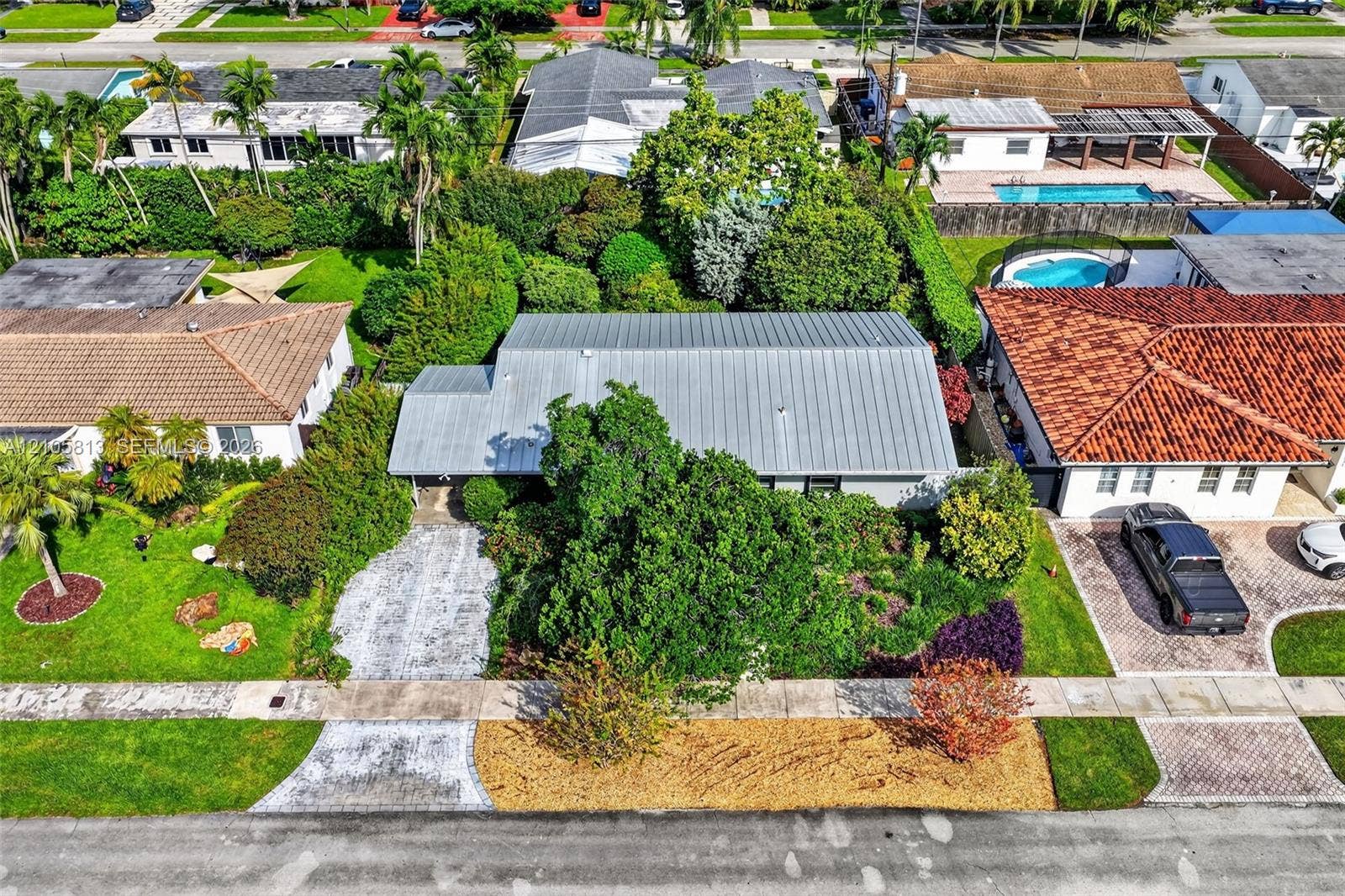 Aerial view of a residential property featuring a metal roof, concrete driveway, and mature landscaping
