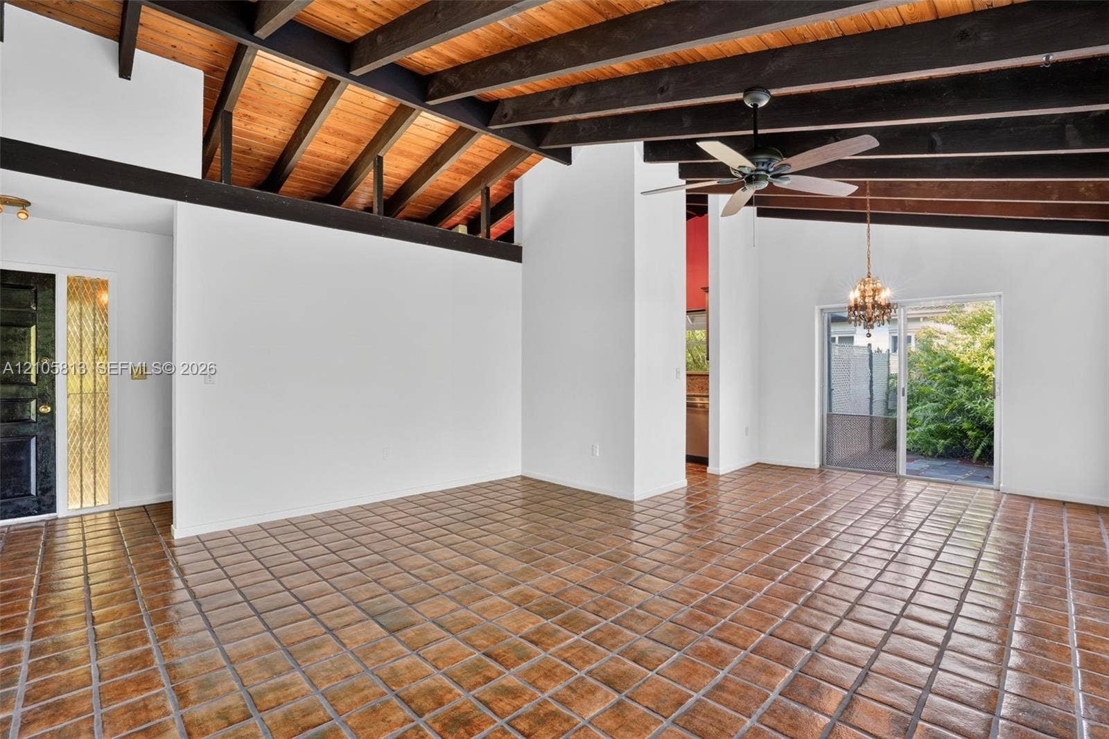 Vaulted ceiling with exposed wood-finish beams, ceramic tile flooring, sliding glass door, and a multi-light chandelier