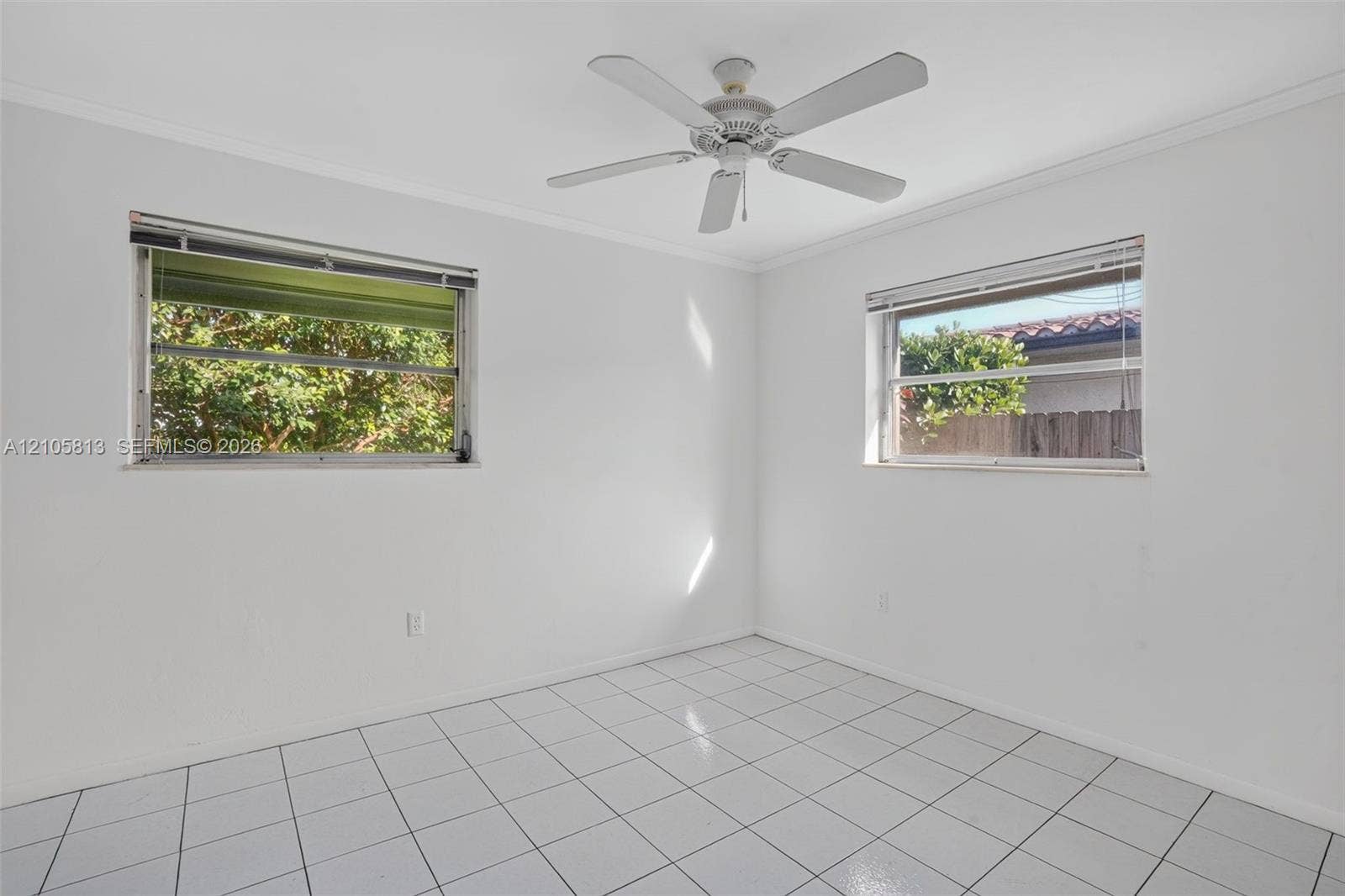 Neutral-toned room featuring tile flooring, white walls, two windows with horizontal blinds, and a white ceiling fan