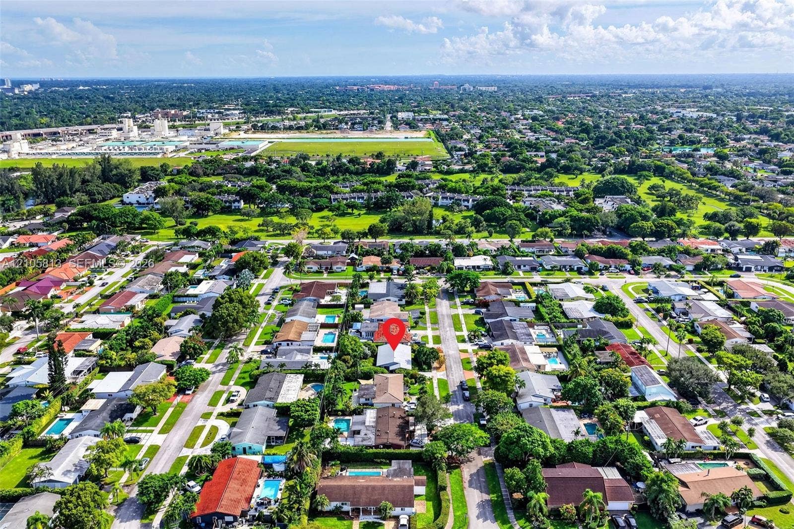 Aerial perspective of a residential property featuring a pitched roof, an established suburban setting with mature trees, and a grid-patterned street layout