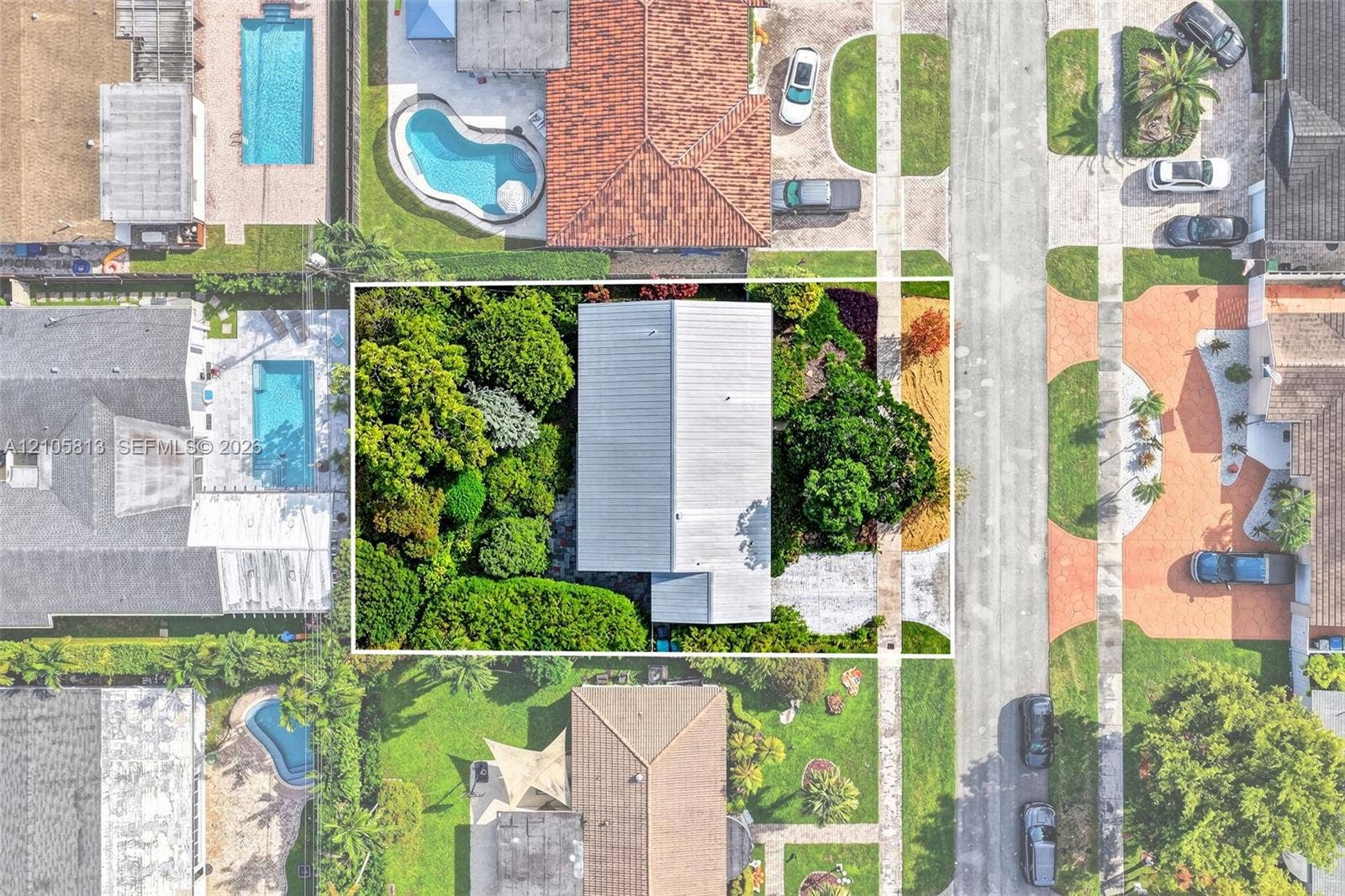 Aerial view of the residential property featuring a metal roof, concrete driveway, and established perimeter landscaping