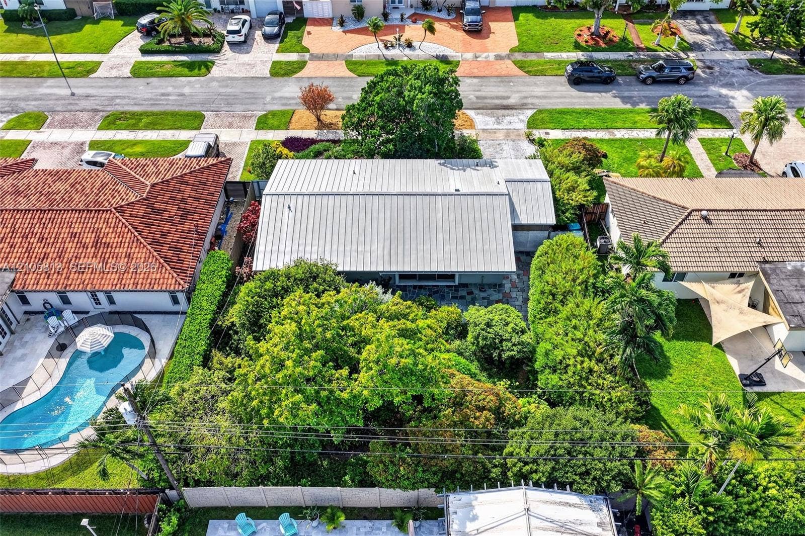 Aerial perspective featuring a metal roof, mature canopy trees, and privacy fencing