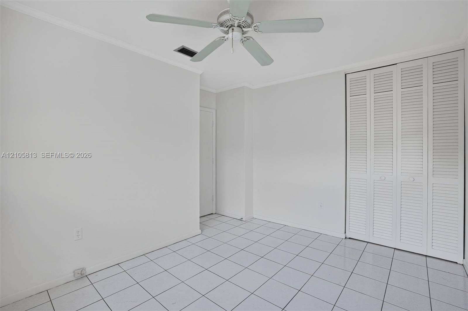 Interior space featuring light-colored tile flooring, white bi-fold closet doors, and a ceiling fan