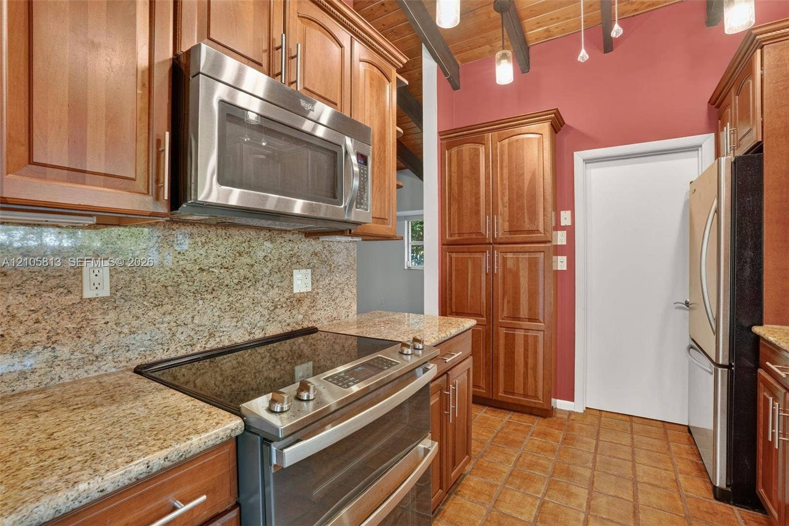Kitchen featuring wood cabinetry, stone countertops, stainless steel appliances, tile flooring, and exposed wood-beam ceiling