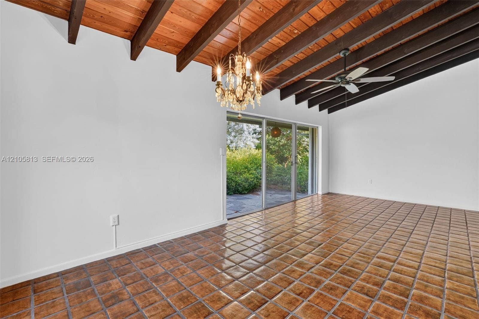 Vaulted ceiling with exposed wood beams, ceramic tile flooring, crystal chandelier, and sliding glass door leading to a patio