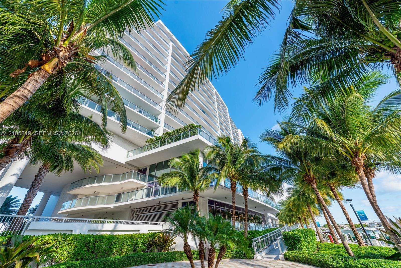 1180 N Federal Highway, #810, Fort Lauderdale, FL 33304 High-rise exterior featuring stepped cantilevered balconies, glass railings, floor-to-ceiling glass windows, and landscaped grounds with mature palm trees