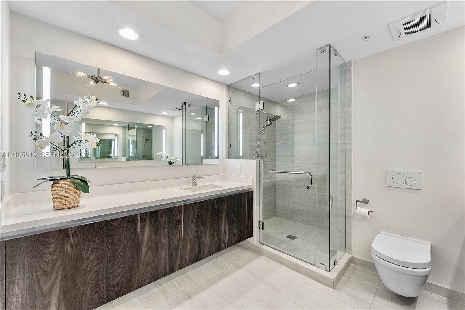 1180 N Federal Highway, #810, Fort Lauderdale, FL 33304 Floating vanity with wood-finish cabinetry, solid surface countertop, expansive wall-mounted mirror, glass-enclosed shower with tiled surround, and wall-mounted toilet