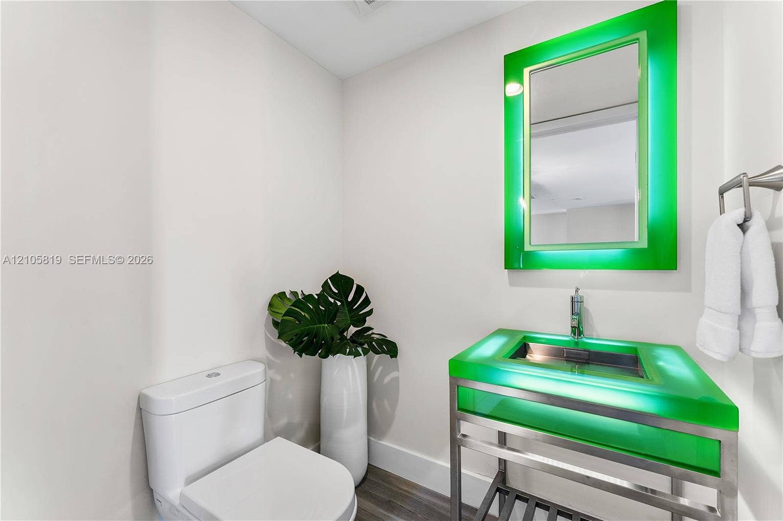 1180 N Federal Highway, #810, Fort Lauderdale, FL 33304 Floating vanity with an integrated green glass sink, polished metal frame, matching illuminated mirror, and wood-finish flooring