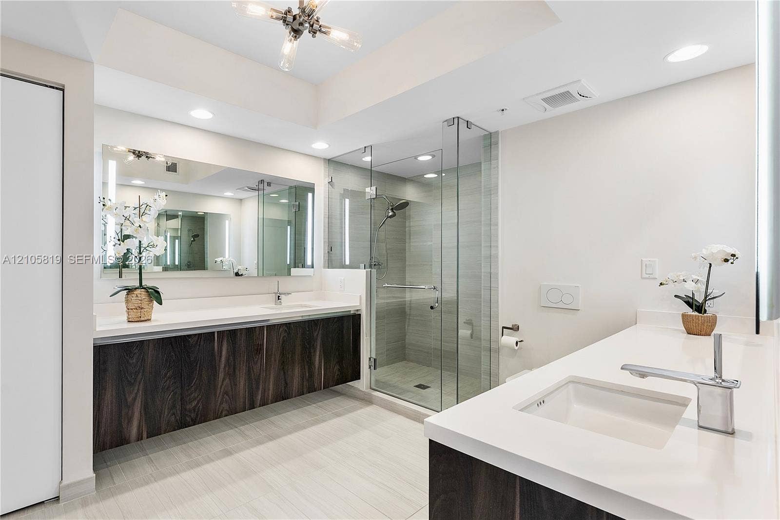 1180 N Federal Highway, #810, Fort Lauderdale, FL 33304 Dual floating vanities featuring dark wood-finish cabinetry, solid surface countertops, integrated rectangular sinks, and chrome fixtures, accompanied by a glass-enclosed walk-in shower with tile surround