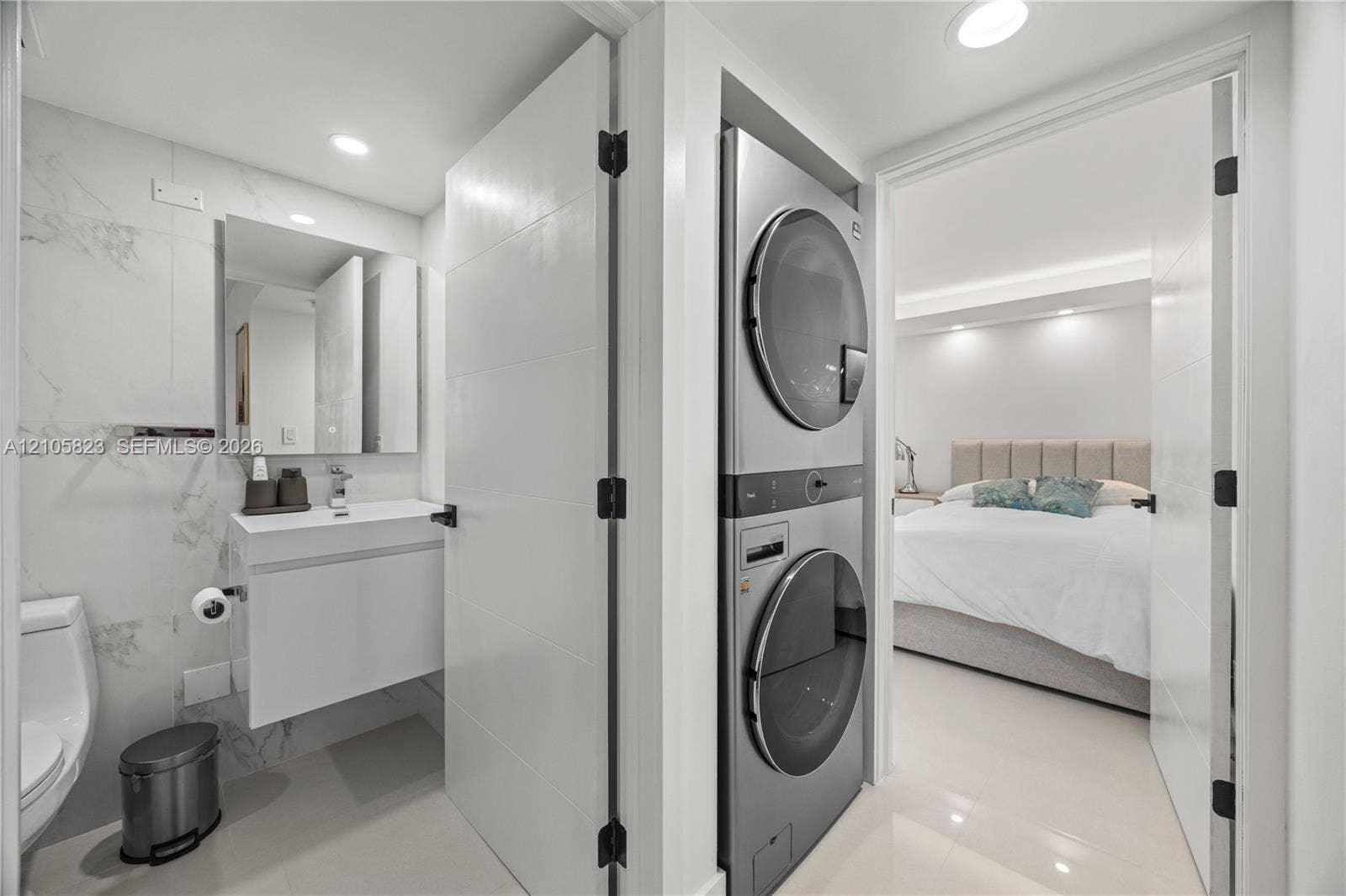 Stacked laundry unit featuring a metallic finish, wall-mounted floating vanity, rectangular vessel sink, and large-format tile wall cladding