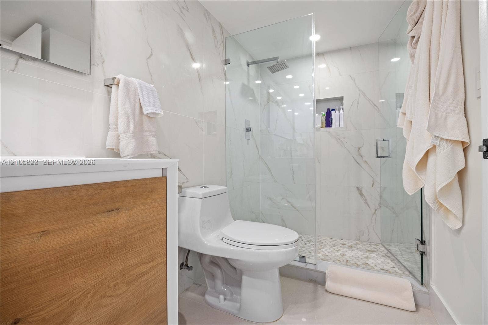 Bathroom featuring a glass-enclosed shower with a built-in recessed niche, stone-finish wall tile, wood-finish vanity cabinetry, and a rainfall showerhead