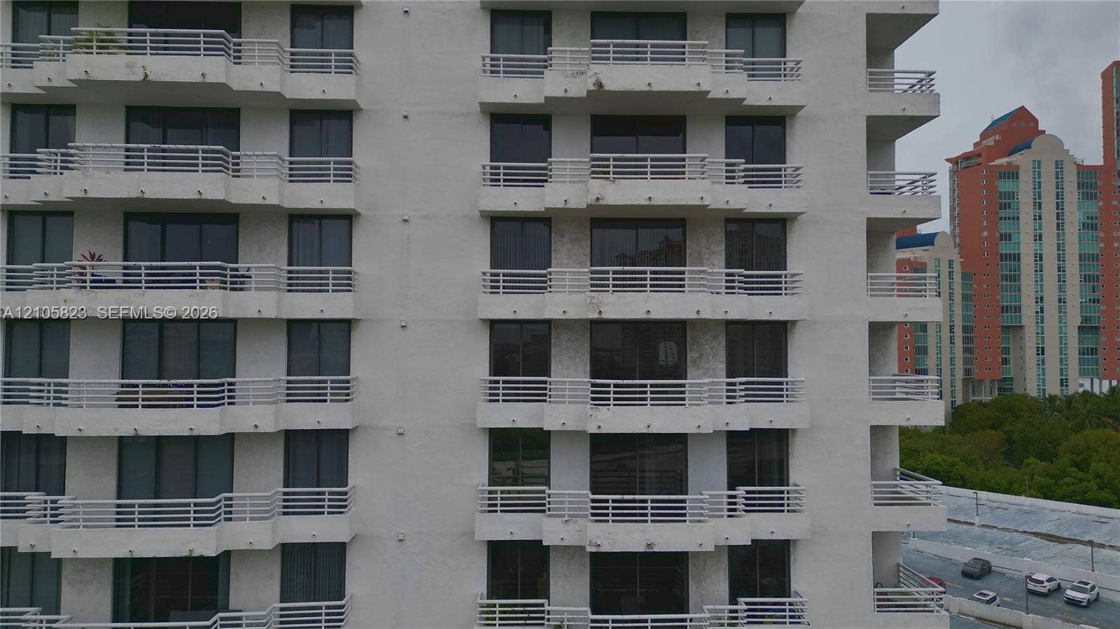 Multi-story exterior featuring white stucco facade, stacked private balconies with horizontal railings, and floor-to-ceiling glass windows