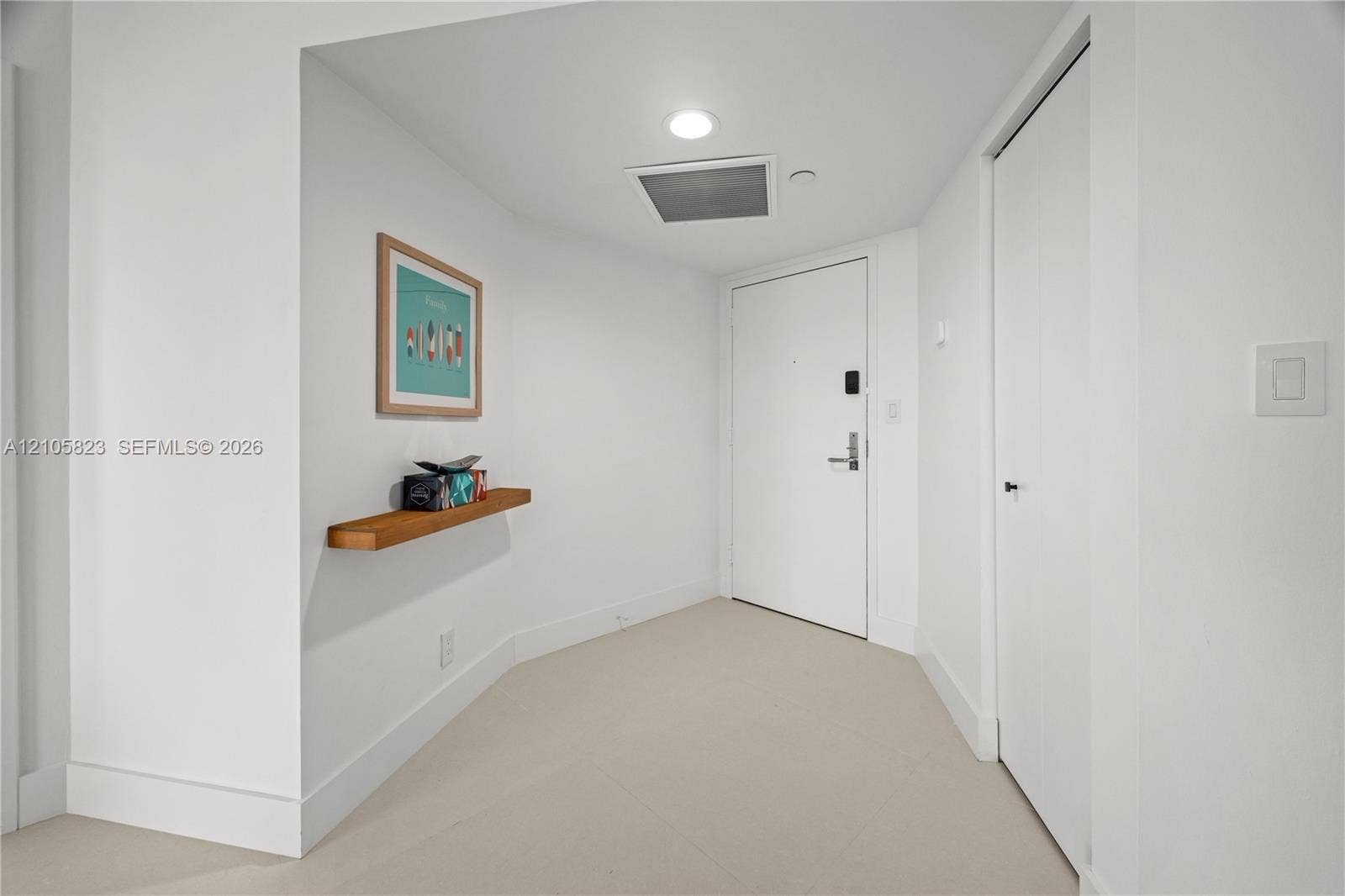 Entryway featuring neutral-toned tile flooring, recessed ceiling lighting, a solid-core door with electronic hardware, and a built-in wood wall-mounted display ledge