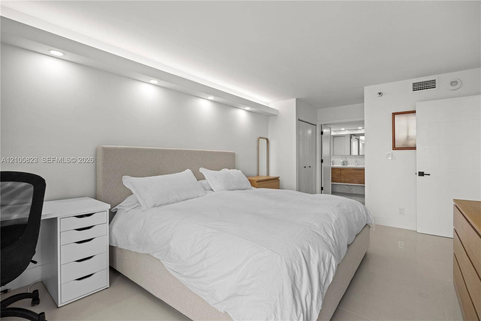 Bedroom featuring recessed soffit lighting, light-toned polished flooring, and a flat-panel interior door with matte black hardware