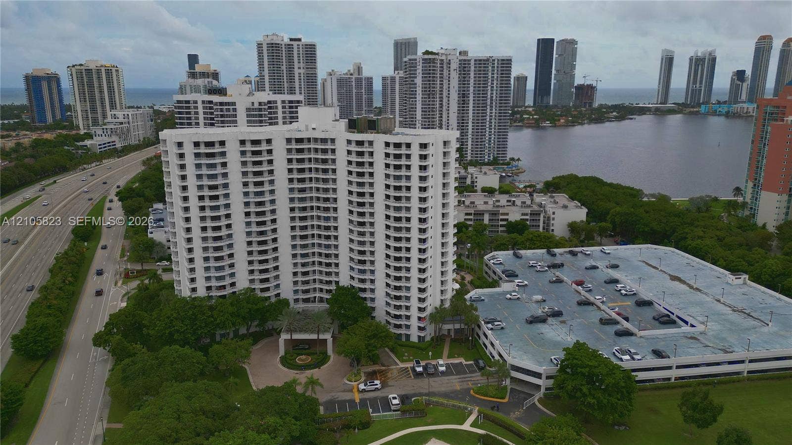 High-rise residential building featuring stacked balconies, a circular porte-cochre, multi-level parking structure, and landscaped grounds