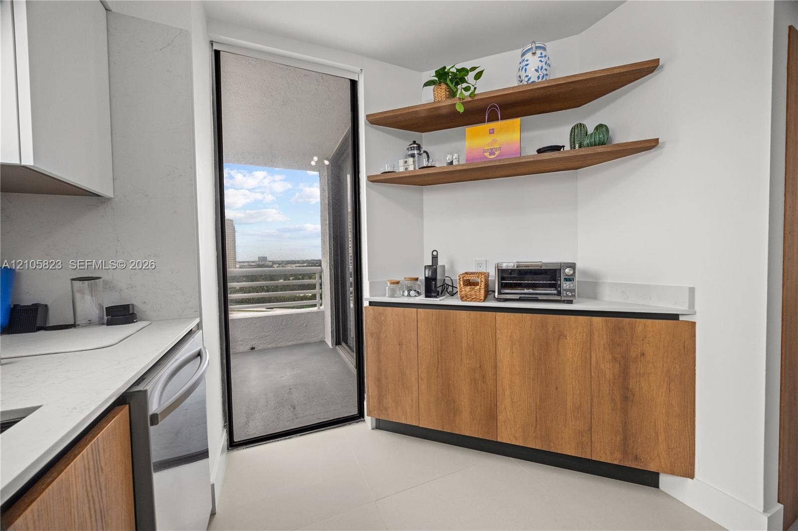 Kitchen area featuring custom wood-finish base cabinetry, quartz countertops, floating wooden wall shelves, and a sliding glass door opening to a private balcony