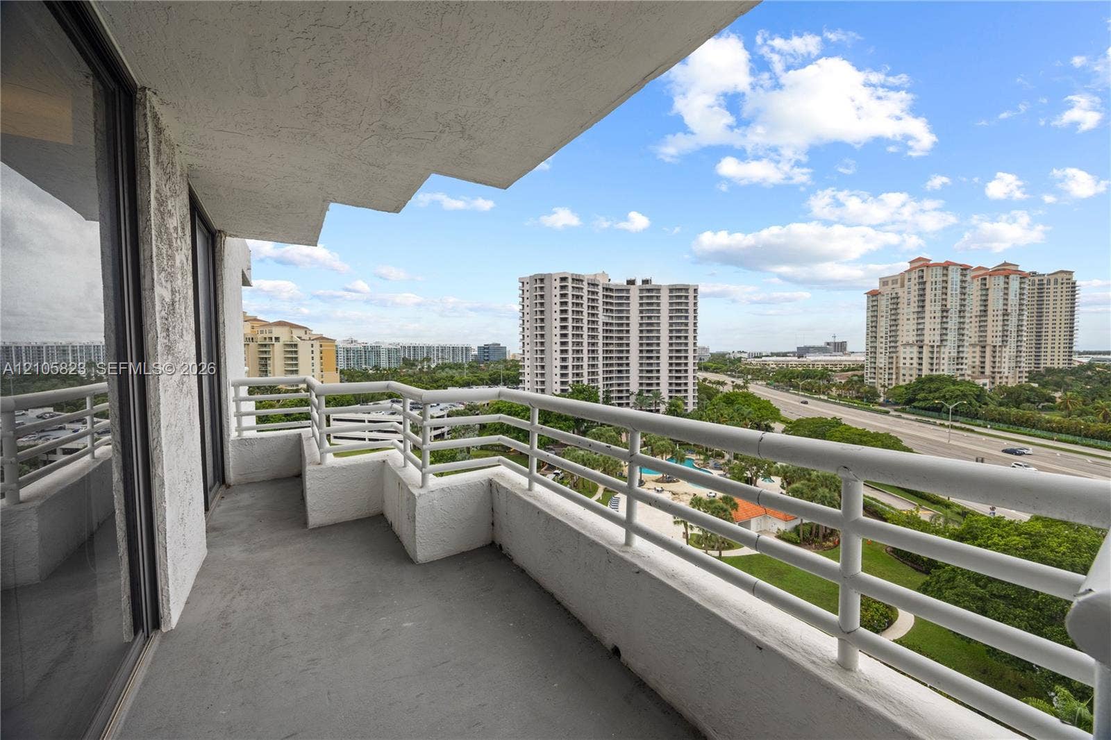 Covered balcony featuring white metal railings, concrete flooring, and sliding glass entry doors