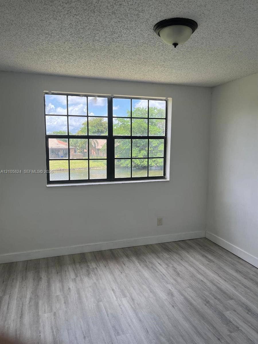 11233 W Atlantic Boulevard, #207, Coral Springs, Coral Springs, FL 33071 Neutral-toned interior space featuring light wood-finish flooring, a multi-pane window with a black frame, and a flush-mount ceiling light