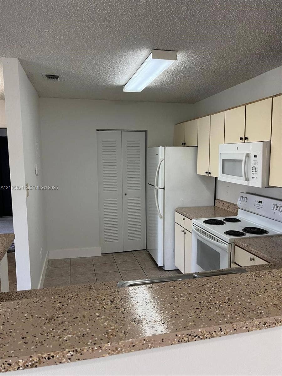 11233 W Atlantic Boulevard, #207, Coral Springs, Coral Springs, FL 33071 Kitchen featuring a speckled stone-finish breakfast bar, tiled flooring, flat-panel cabinetry, and built-in white appliances including a range and over-the-range microwave