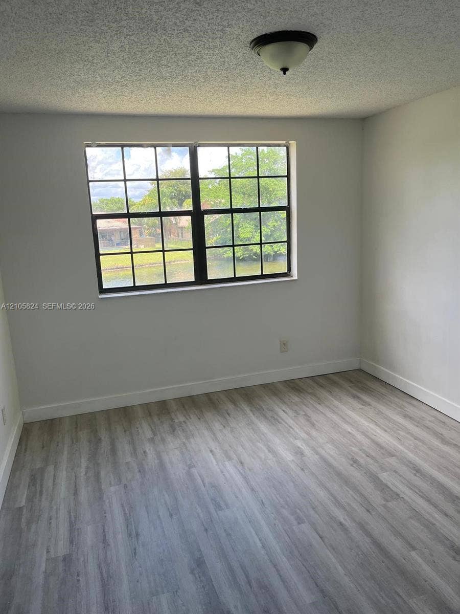 11233 W Atlantic Boulevard, #207, Coral Springs, Coral Springs, FL 33071 Room with wood-finish flooring, neutral wall paint, grid-pane window, and a flush-mount ceiling fixture