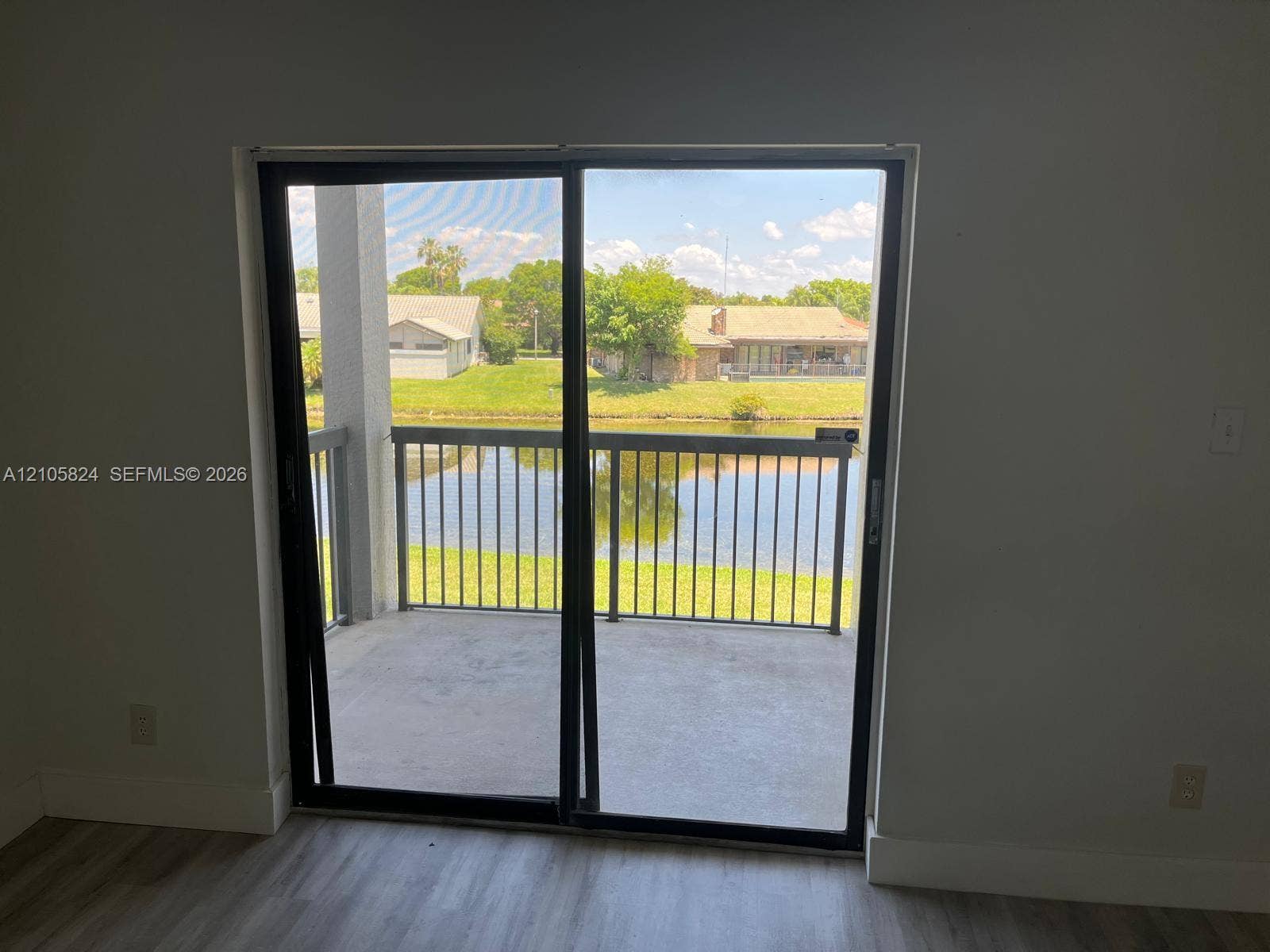 11233 W Atlantic Boulevard, #207, Coral Springs, Coral Springs, FL 33071 Sliding glass door opening to a covered balcony with metal railing, wood-finish flooring, and water frontage