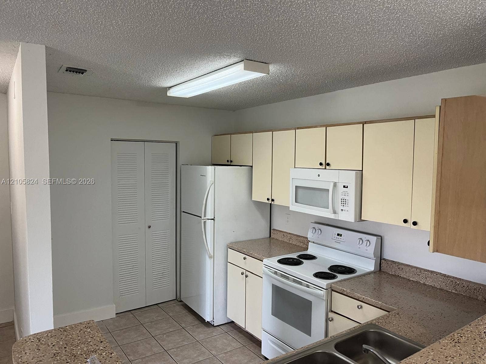 11233 W Atlantic Boulevard, #207, Coral Springs, Coral Springs, FL 33071 Kitchen featuring light-finish cabinetry, neutral solid-surface countertops, dual-basin stainless steel sink, and white appliances including an electric range and built-in microwave