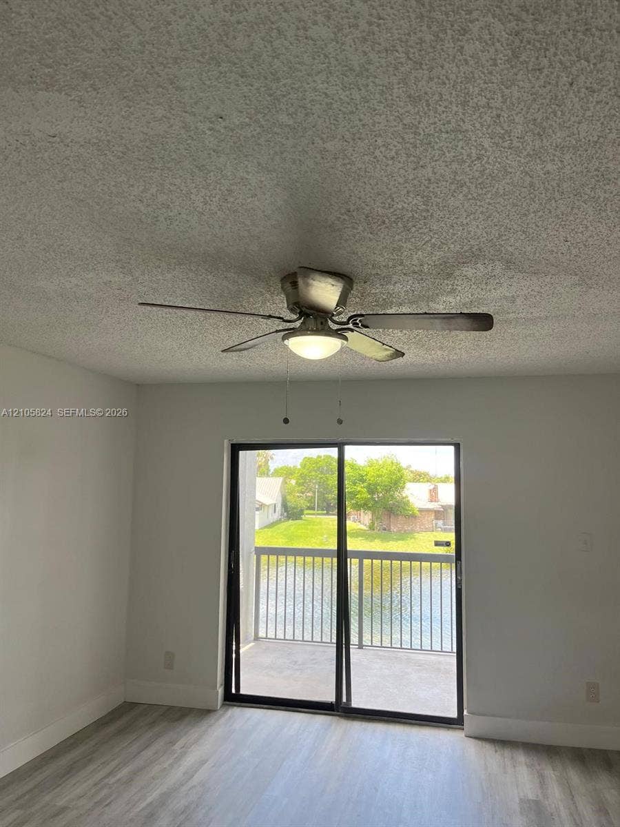 11233 W Atlantic Boulevard, #207, Coral Springs, Coral Springs, FL 33071 Wood-finish flooring, ceiling fan with integrated light fixture, and glass sliding door providing outdoor balcony access with waterfront scenery