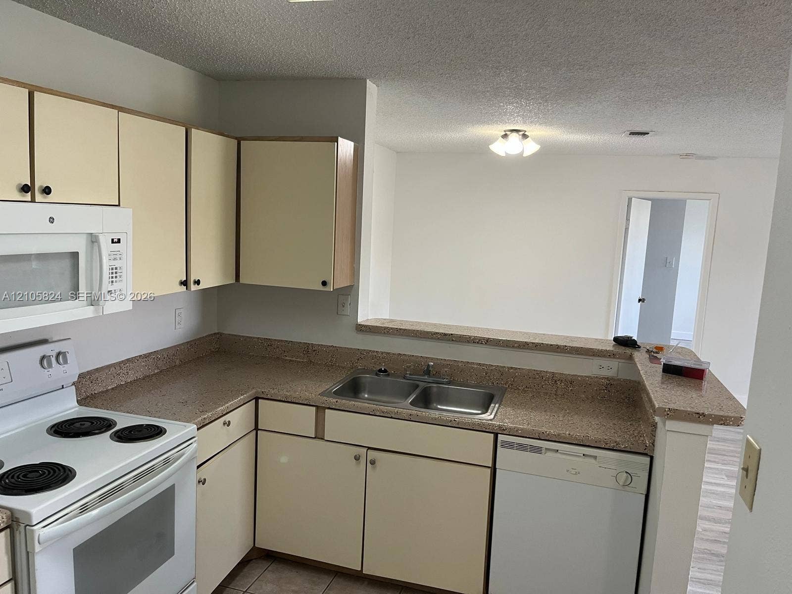11233 W Atlantic Boulevard, #207, Coral Springs, Coral Springs, FL 33071 Kitchen featuring light-finish cabinetry, stone-texture laminate countertops, dual-basin stainless steel sink, and white appliances including a built-in microwave and dishwasher