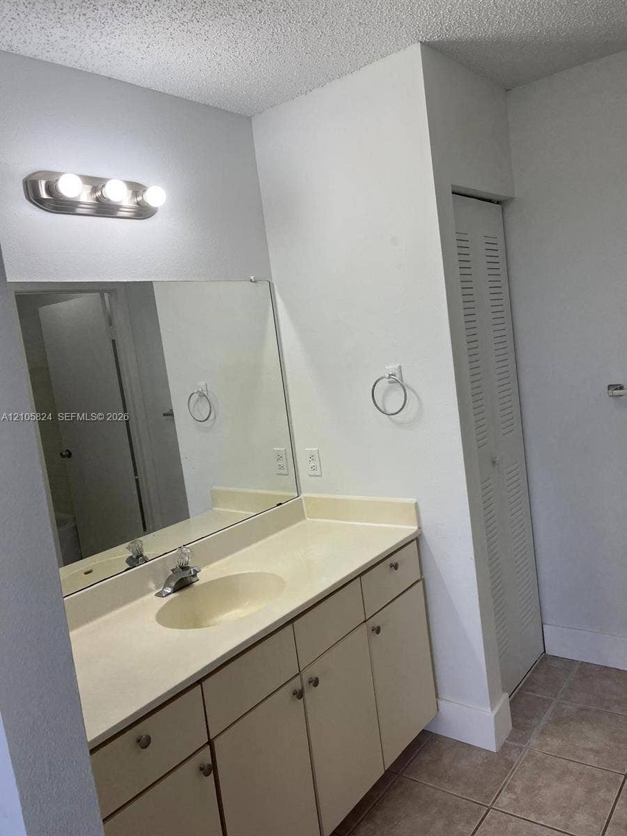 11233 W Atlantic Boulevard, #207, Coral Springs, Coral Springs, FL 33071 Single-vanity cabinet with an integrated countertop and basin, large-format vanity mirror, three-bulb wall-mounted lighting fixture, and tile flooring