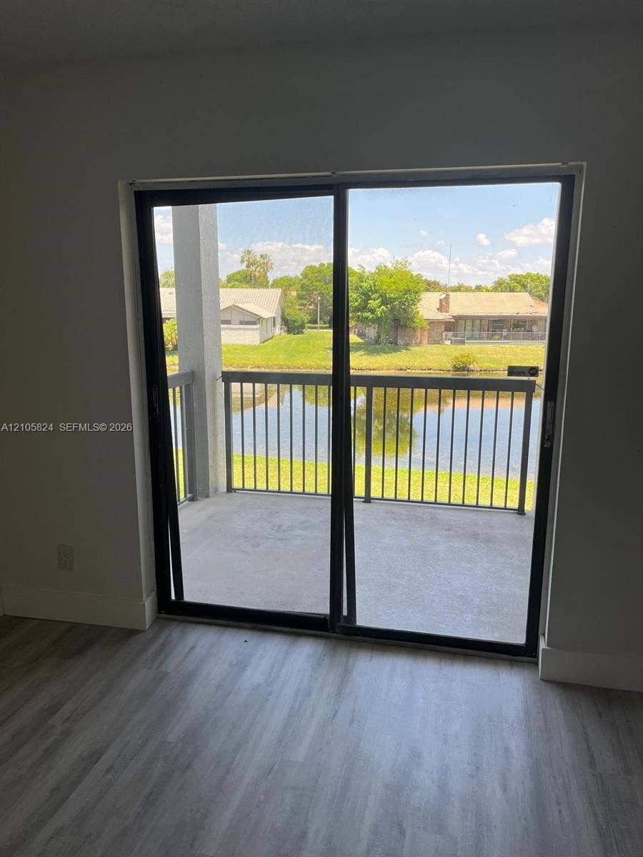 11233 W Atlantic Boulevard, #207, Coral Springs, Coral Springs, FL 33071 Sliding glass door opening to a concrete balcony with dark metal railings, wood-finish flooring, and water frontage