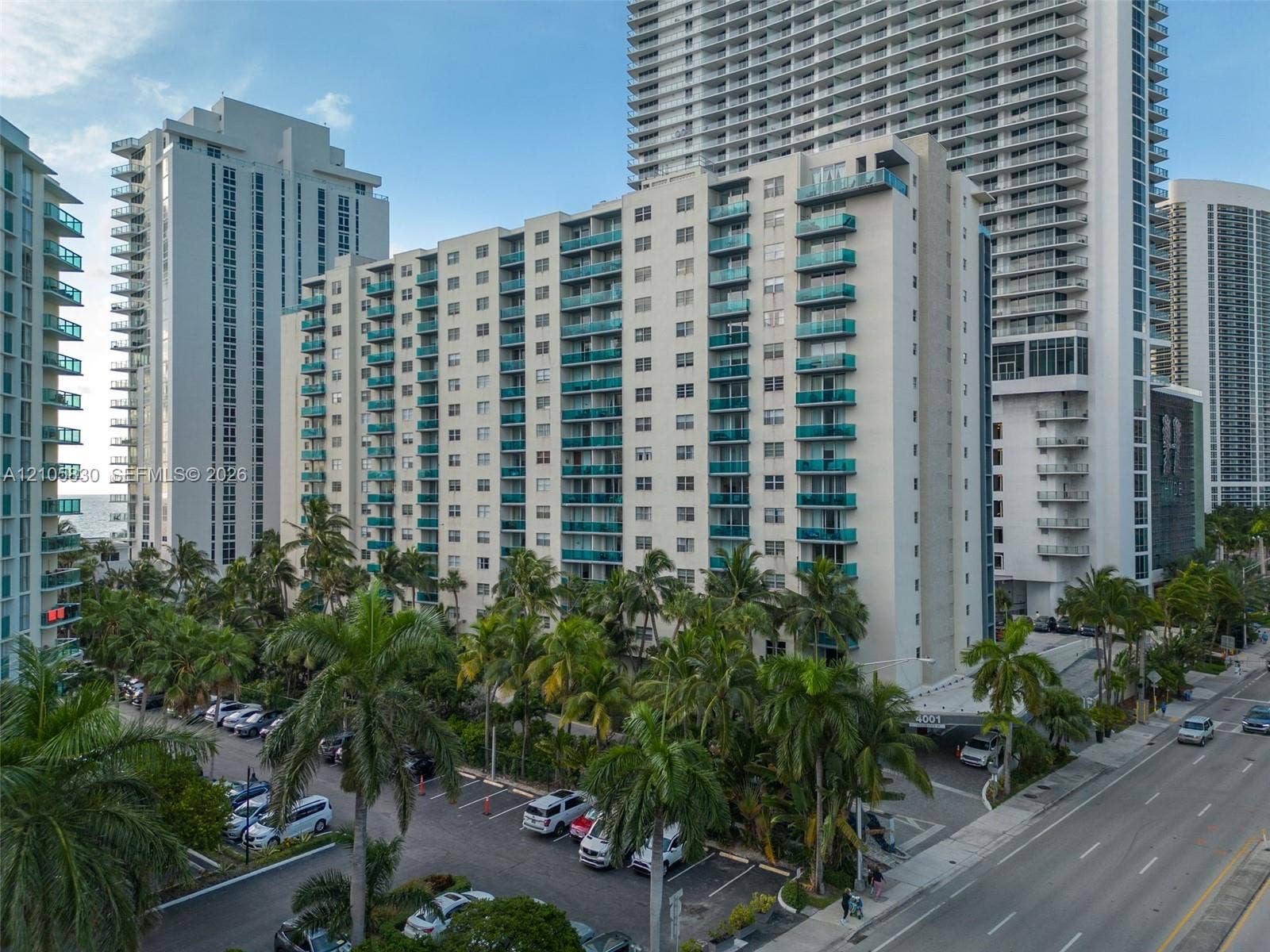 4001 S Ocean Drive, #14F, Hollywood, Hollywood, FL 33019 High-rise building exterior featuring private balconies with glass railings, paved surface parking, and mature palm landscaping