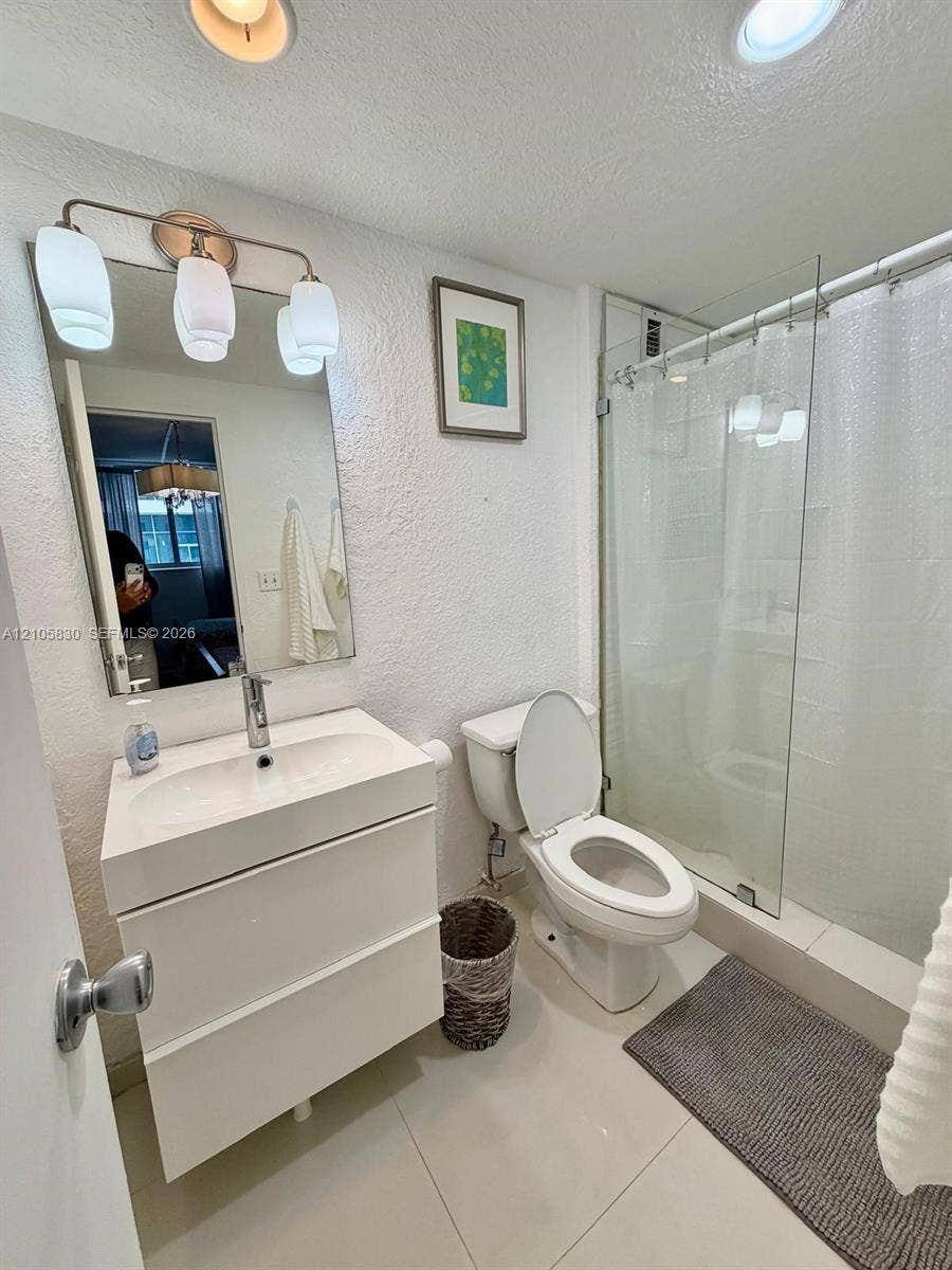 4001 S Ocean Drive, #14F, Hollywood, Hollywood, FL 33019 Modern floating vanity with an integrated sink and chrome faucet, rectangular wall mirror, three-light fixture, and a glass-enclosed shower featuring tile surround