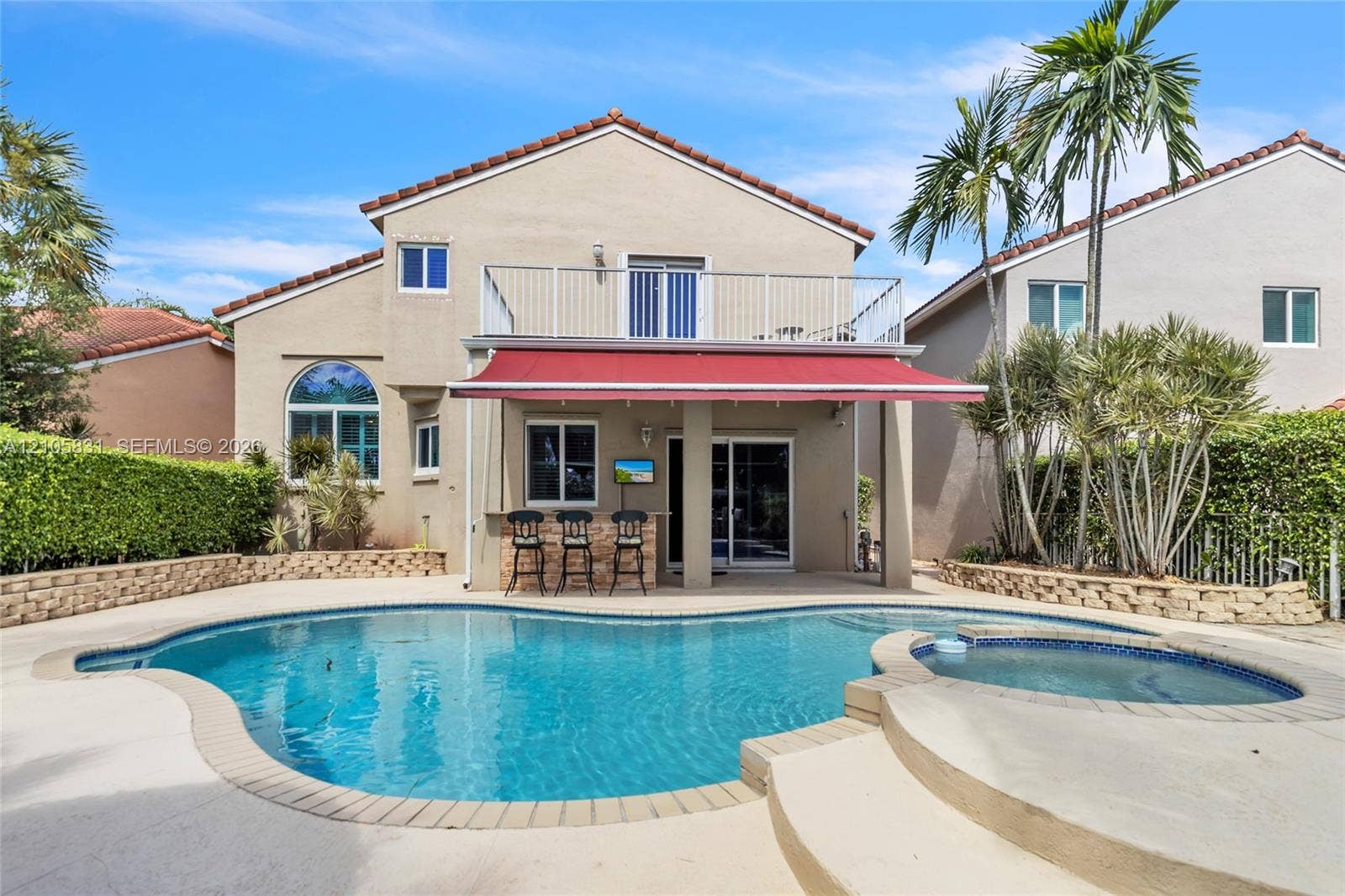 15612 SW 16th Court, Pembroke Pines, FL 33027 Stucco exterior featuring an in-ground swimming pool, integrated spa, retractable patio awning, and a second-story balcony with metal railing