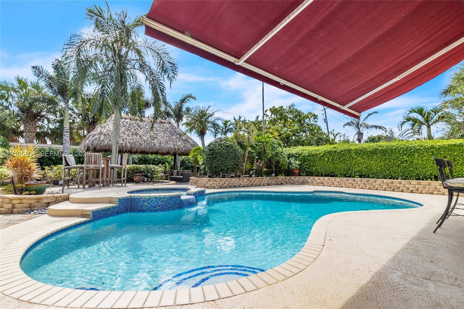 15612 SW 16th Court, Pembroke Pines, FL 33027 In-ground pool with stone coping and integrated spa, retractable awning, detached thatch-roofed cabana, and tiered stone retaining walls
