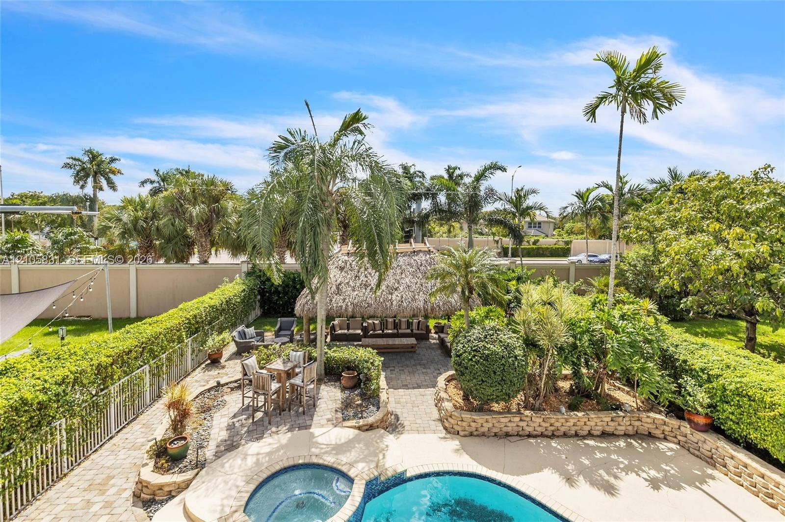 15612 SW 16th Court, Pembroke Pines, FL 33027 Backyard featuring a custom swimming pool with integrated spa, paved stone patio, thatched-roof cabana, stone retaining walls, and mature palm trees