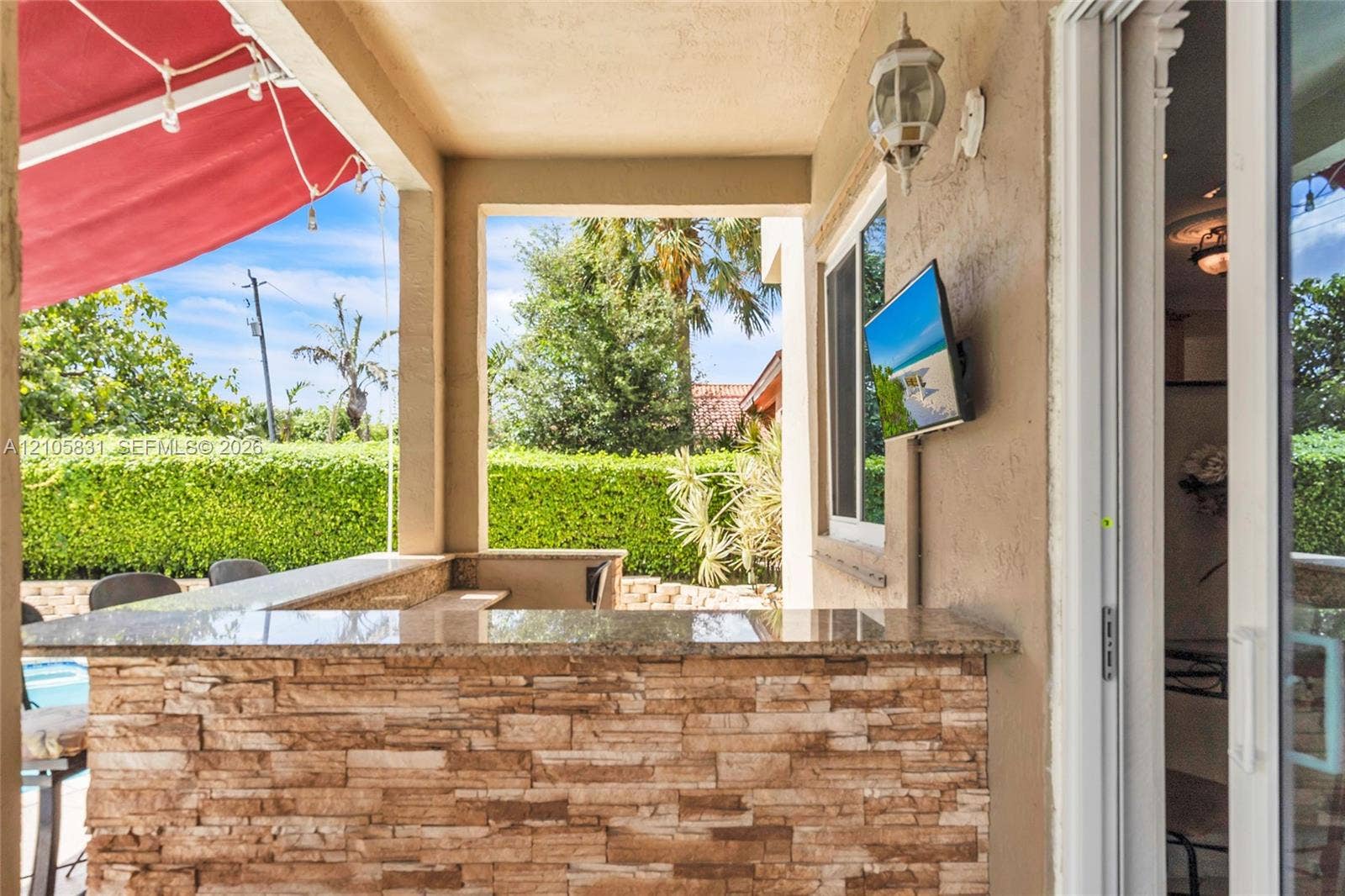 15612 SW 16th Court, Pembroke Pines, FL 33027 Covered patio featuring a stacked stone bar with a solid surface countertop, wall-mounted television, and exterior sconce lighting