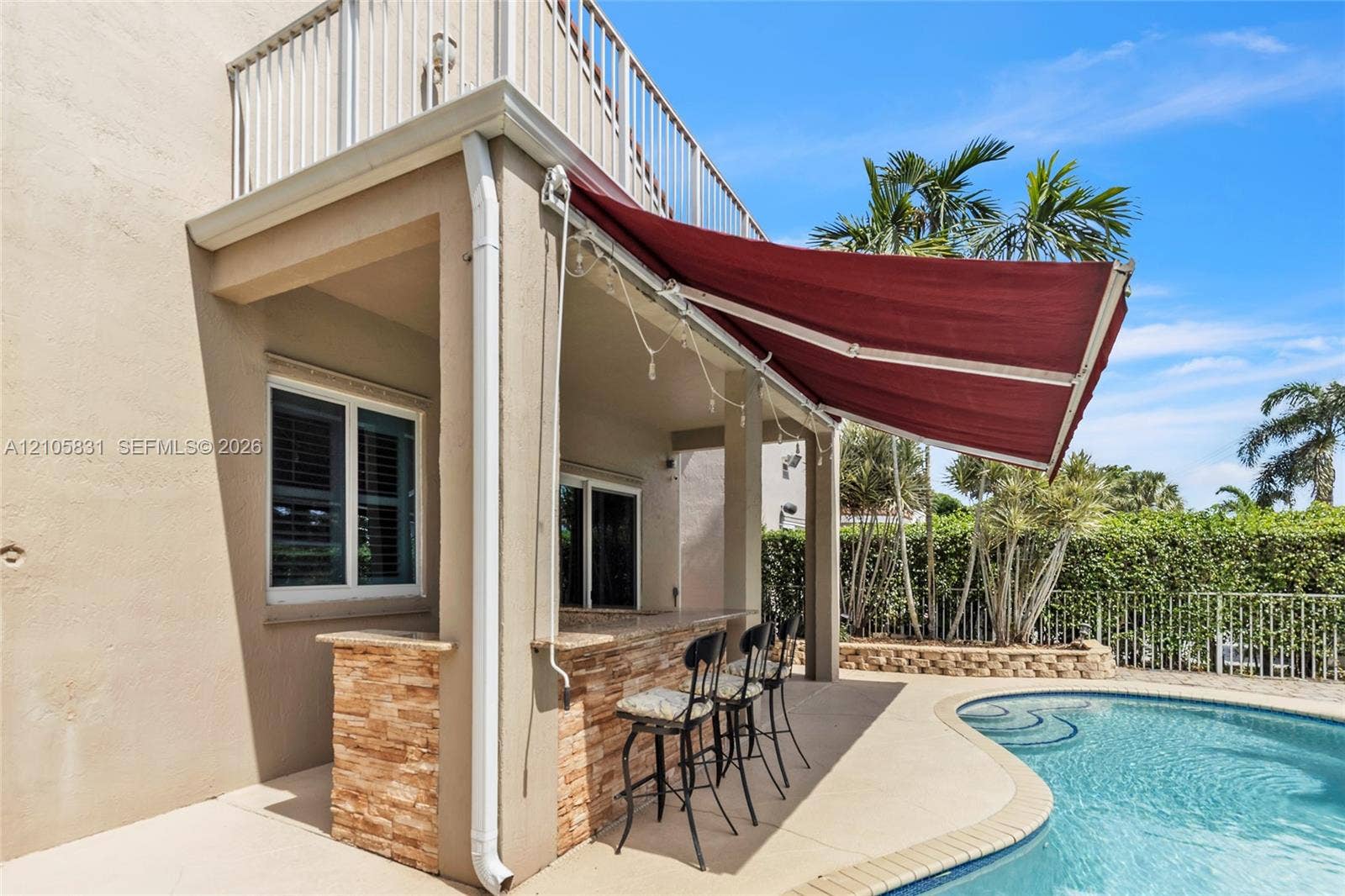 15612 SW 16th Court, Pembroke Pines, FL 33027 Covered outdoor patio featuring a stacked stone bar, retractable fabric awning, second-level balcony with white railings, and swimming pool