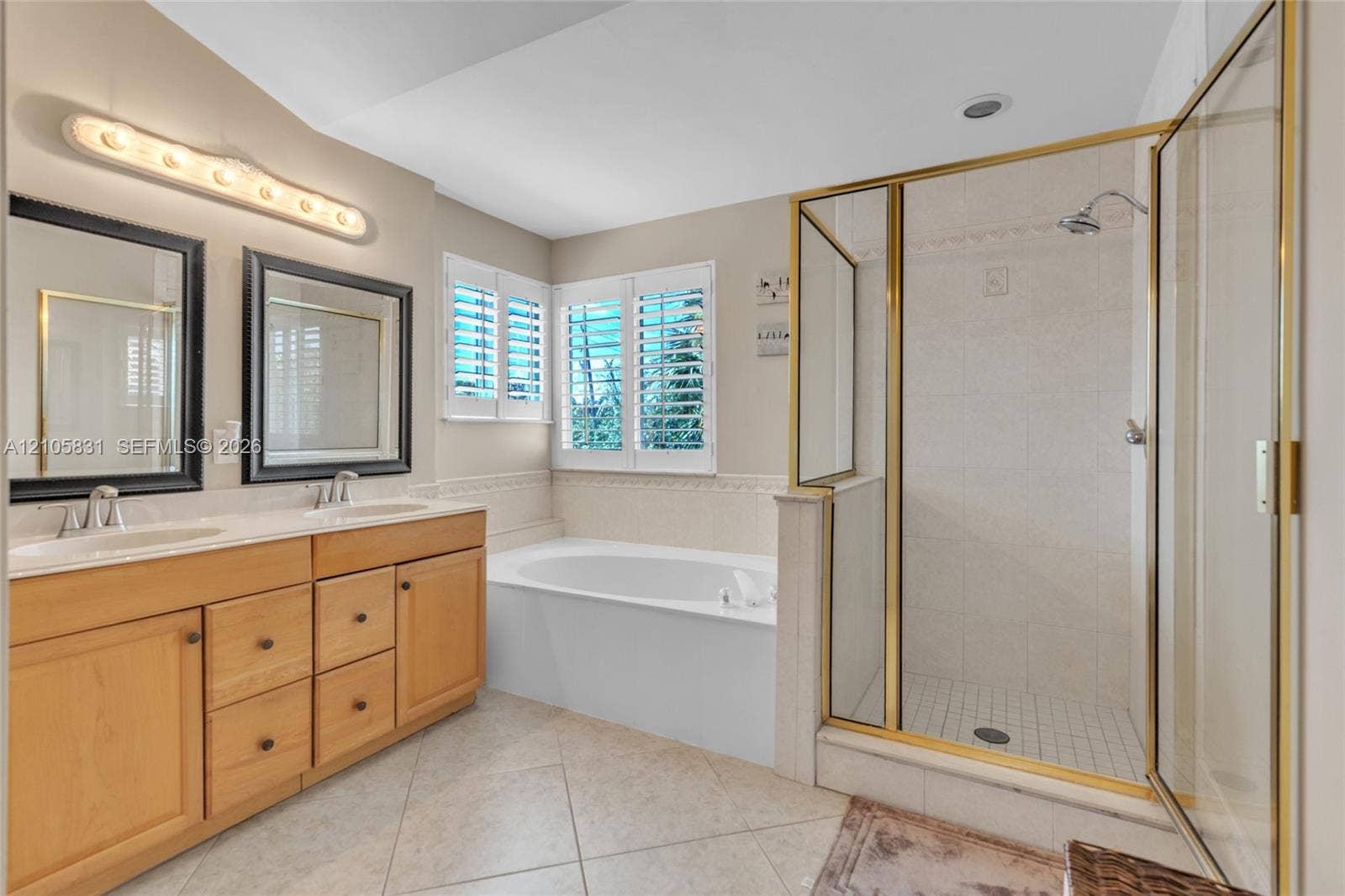 15612 SW 16th Court, Pembroke Pines, FL 33027 Bathroom featuring dual-sink wood cabinetry, a recessed soaking tub, a tiled walk-in shower with gold-finish frame, and white plantation shutters