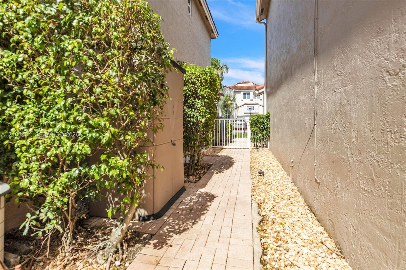 15612 SW 16th Court, Pembroke Pines, FL 33027 Side yard featuring a paver walkway, decorative stone ground cover, and a white metal gate