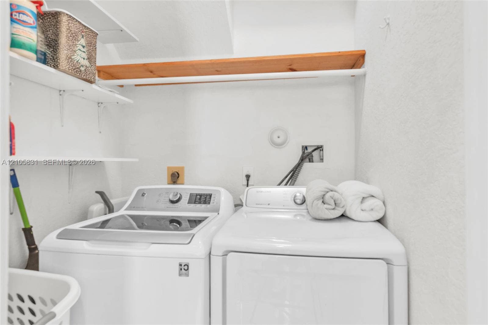 15612 SW 16th Court, Pembroke Pines, FL 33027 Laundry area featuring white top-loading washer and dryer, mounted wood-finish shelving, and wall-mounted plumbing hookups