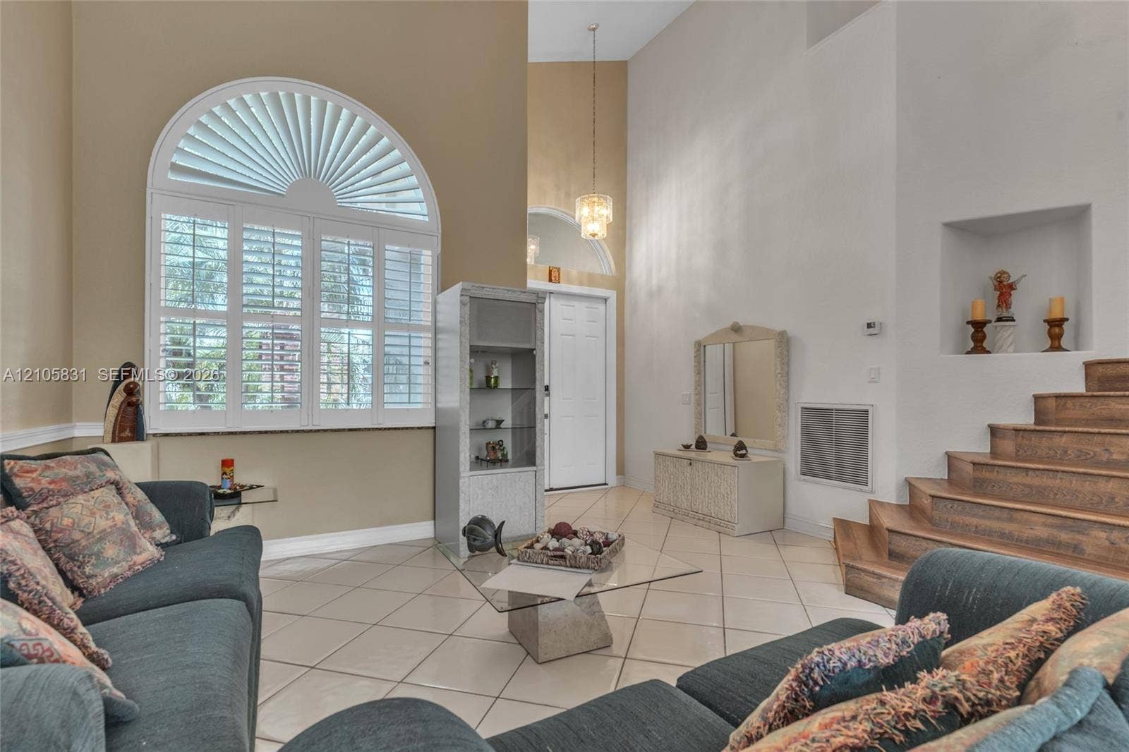 15612 SW 16th Court, Pembroke Pines, FL 33027 High-ceilinged living space featuring an arched window with plantation shutters, tile flooring, a recessed wall niche, and wood-finish stairs