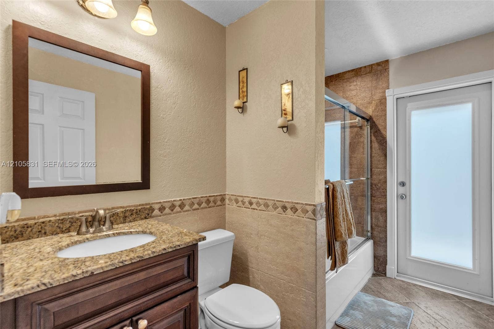 15612 SW 16th Court, Pembroke Pines, FL 33027 Bathroom featuring a wood-finish vanity with a stone-composite countertop, integrated sink, framed wall mirror, half-wall tile wainscoting with decorative accent border, and a glass-enclosed shower