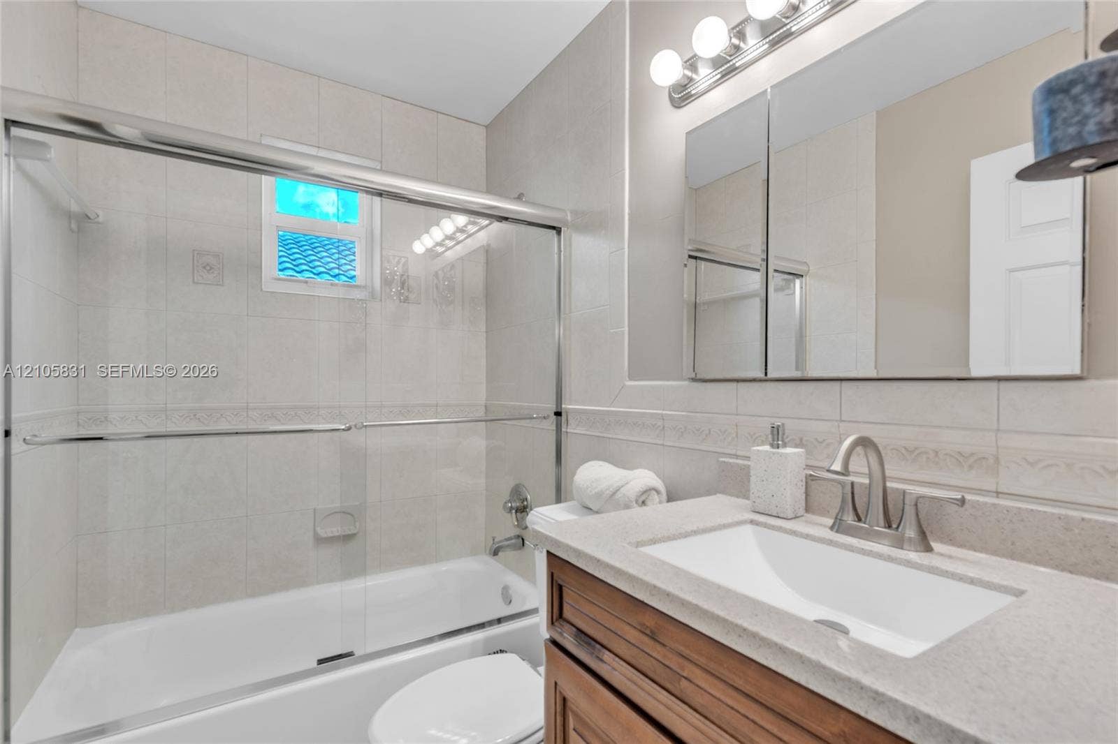 15612 SW 16th Court, Pembroke Pines, FL 33027 Bathroom featuring a vanity with stone-finish countertop and undermount sink, a tiled tub-shower combination with glass sliding doors, and a multi-bulb light fixture