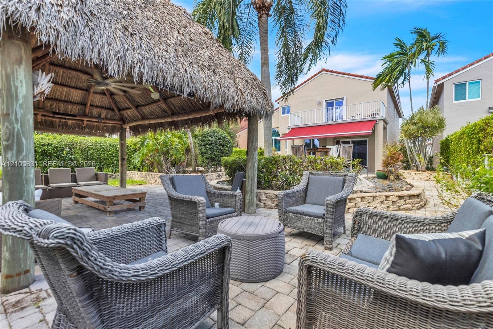 15612 SW 16th Court, Pembroke Pines, FL 33027 Outdoor living space featuring a thatched-roof tiki hut, paver patio, tiered stone retaining wall, and mature landscaping